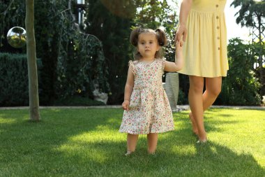 Anne, parkta yeşil çimlerde yürümeyi öğrenirken bebeğe destek oluyor.