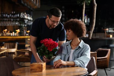 Uluslararası ilişkiler. Yakışıklı bir adam kafede sevgilisine güller sunuyor.