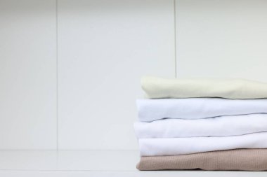 Beyaz rafta katlanmış farklı tişörtlerin yığını, yazı için yer. Giysileri düzenleme