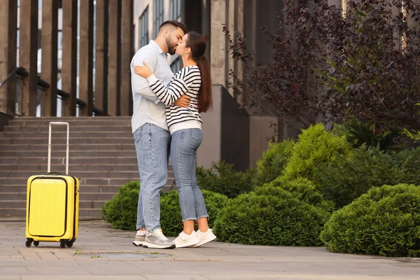 Long-distance relationship. Beautiful young couple kissing and suitcase near building outdoors