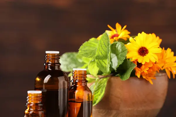 Bottles with essential oils, mint and flowers on blurred background, closeup