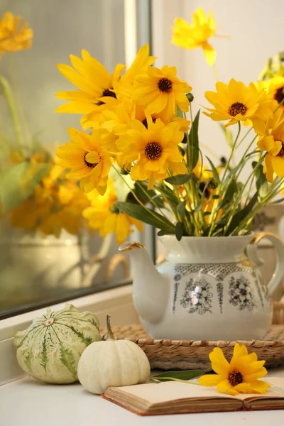 Composition with beautiful flowers, pumpkins and book on windowsill. Autumn atmosphere