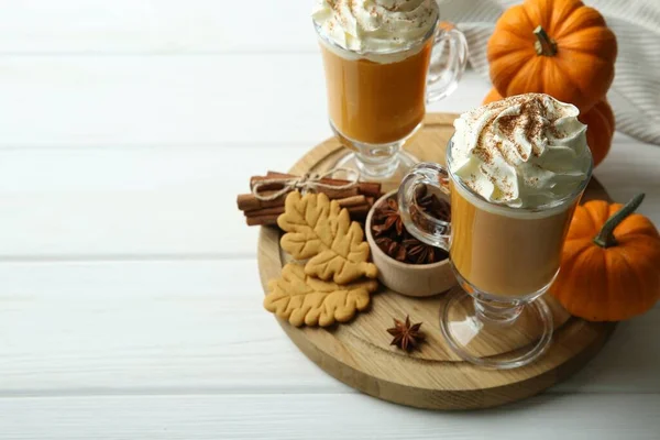 Tasty pumpkin latte with whipped cream in glasses, spices and cookies on white wooden table. Space for text