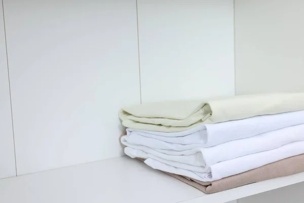Stack of different folded shirts on white shelf, space for text. Organizing clothes