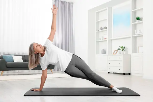 stock image Senior woman practicing yoga on mat at home