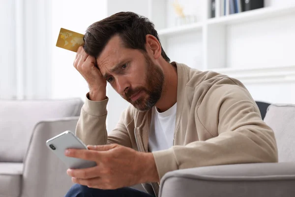 Zdenerwowany Człowiek Kartą Kredytową Pomocą Smartfona Fotelu Domu Uważaj Oszustwo — Zdjęcie stockowe