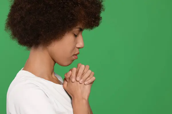 Woman with clasped hands praying to God on green background. Space for text