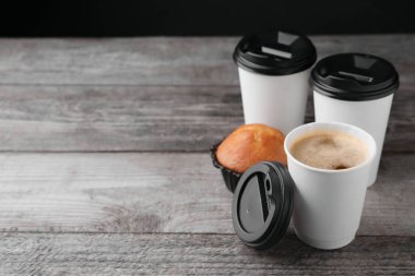 Paket kahve. Kağıt bardaklarda lezzetli içecekler ve ahşap masada çörekler, mesaj için yer var.