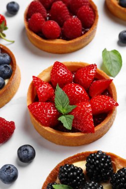 Tartlets with different fresh berries on white table. Delicious dessert clipart