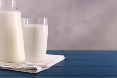 Mavi ahşap masada sürahi ve bir bardak taze süt, metin için yer var.