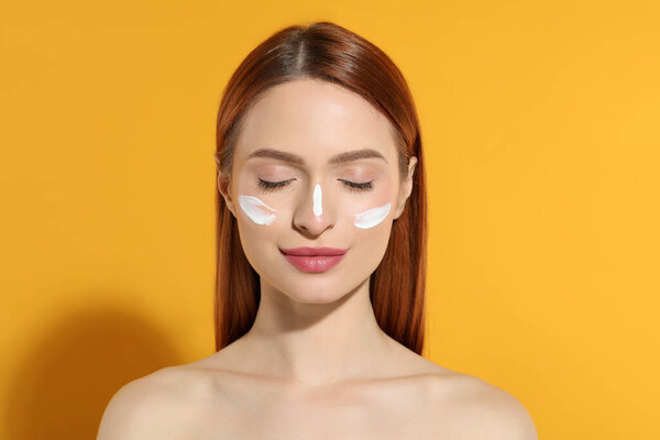 Beautiful young woman with sun protection cream on her face against orange background