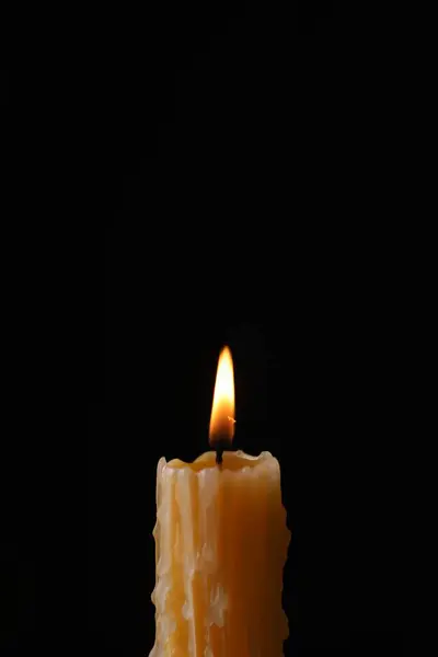 Burning church wax candle on black background