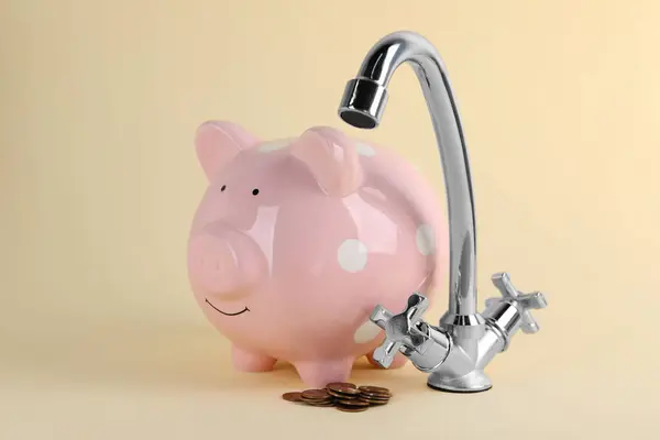 Water scarcity concept. Piggy bank, tap and coins on beige background