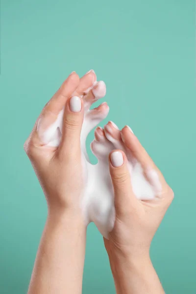 Woman washing hands with cleansing foam on green background, closeup. Skin care cosmetic