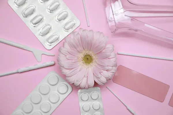 Gynecological treatment. Sterile tools, pills and gerbera flower on pink background, flat lay