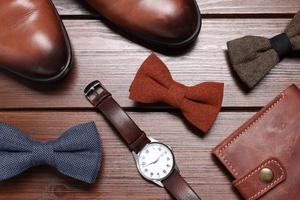 Stylish color bow ties, shoes, wallet and wristwatch on wooden background, flat lay