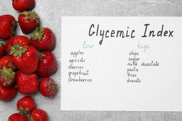 List with products of low and high glycemic index and strawberries on light grey table, top view
