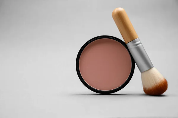 Open face powder and brush on light grey background. Space for text