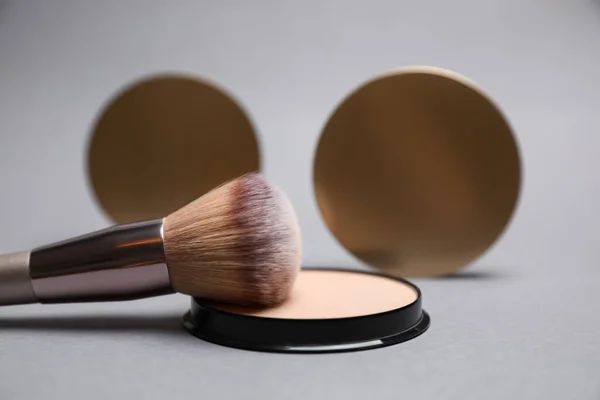 Open face powder and brush on light grey background, closeup