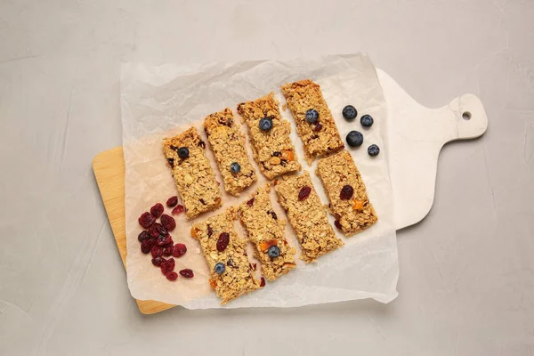 Tasty granola bars, dried cherries and blueberries on light gray textured table, top view