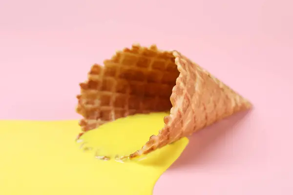 Melted ice cream and wafer cone on pink background, closeup