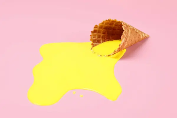 Melted ice cream and wafer cone on pink background