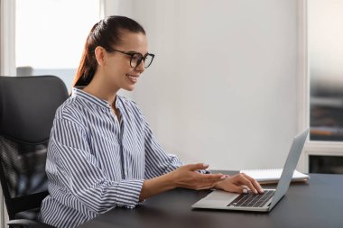 Ofisteki siyah masada modern laptop kullanan mutlu bir kadın.