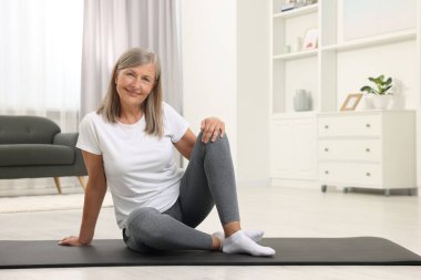 Evde paspasın üzerinde oturan mutlu yaşlı kadın, mesaj için yer var. Yoga alıştırması.