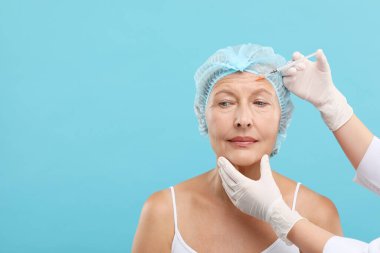 Doktor, açık mavi arka planda yaşlı kadına yüz enjeksiyonu yapıyor. Mesaj için yer var. Estetik ameliyat