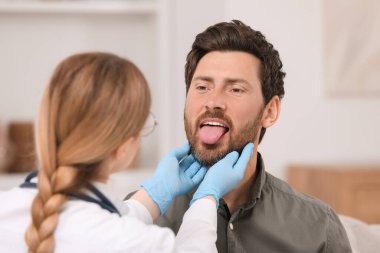 Eldivenli doktor içeride adamın ağız boşluğunu inceliyor.