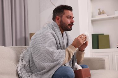 Evdeki kanepede battaniyeye sarılı hasta bir adam. Soğuk belirtileri