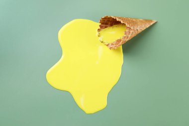 Yeşil arka planda erimiş dondurma ve gofret külahı.