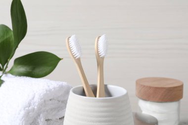 Bambu diş fırçaları tutacakta, yumuşak havlu ve hafif arka planda yapraklar, yakın plan.