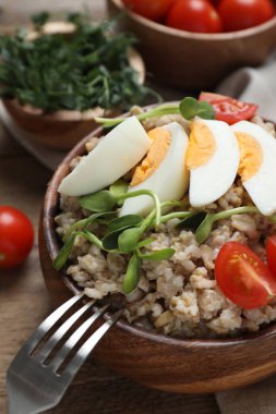 Yumurtalı, domatesli ve mikroyeşillikli kaynamış yulaf ezmesi ahşap masada servis edilir.