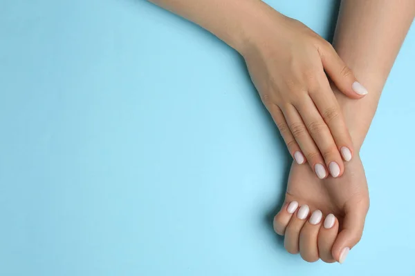 Woman showing her manicured hands with white nail polish on light blue background, top view. Space for text