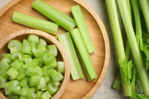Many fresh cut celery stalks and leaves on wooden table, flat lay