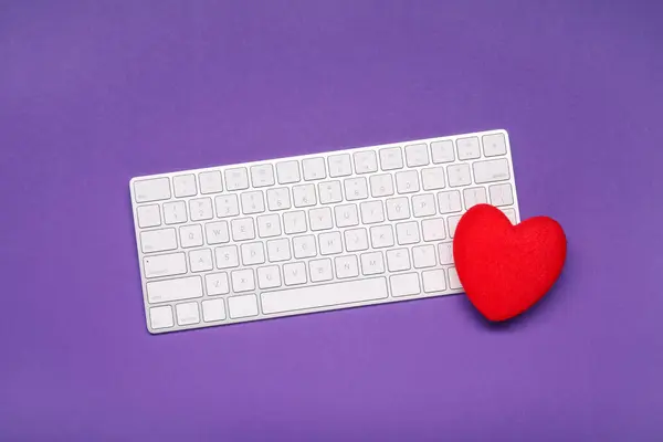 Long-distance relationship concept. Keyboard and decorative heart on violet background, top view