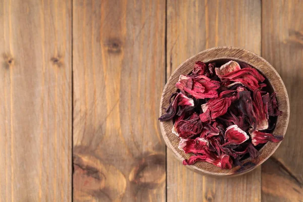 Dry hibiscus tea in bowl on wooden table, top view. Space for text