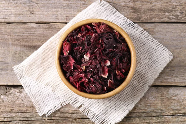 Dry hibiscus tea in bowl on wooden table, top view