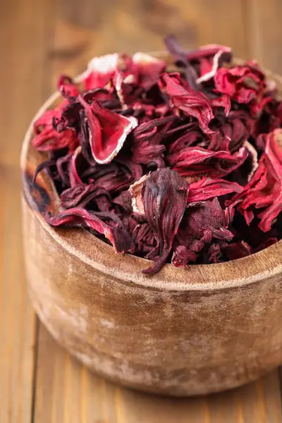 Dry hibiscus tea in bowl on wooden table, closeup