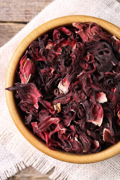 Dry hibiscus tea in bowl on wooden table, top view