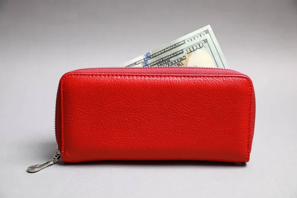 Stylish red leather purse with dollar banknotes on light grey background