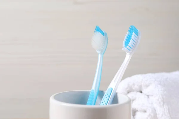 Plastic toothbrushes in holder against light background, closeup. Space for text