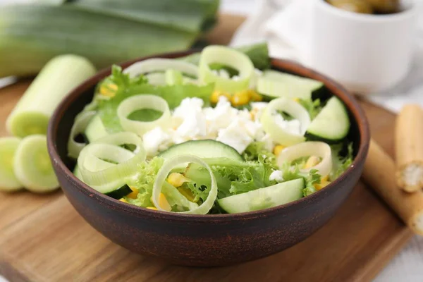 Bowl of tasty salad with leek and cheese on table, closeup