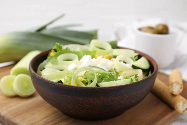 Bowl of tasty salad with leek and cheese on table, closeup