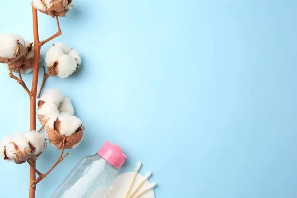 Bottle of makeup remover, cotton flowers, pad and swabs on light blue background, flat lay. Space for text