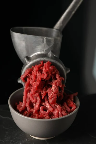 Metal meat grinder with beef mince on dark textured table against black background, closeup