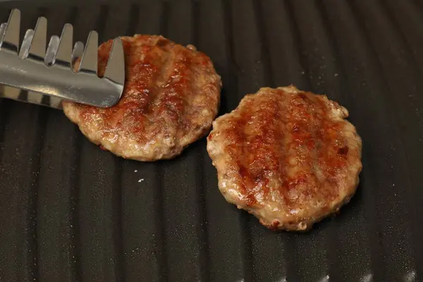 Taking delicious hamburger patty with tongs from grill pan, closeup