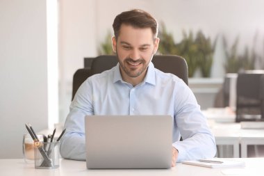 Ofisteki beyaz masada modern laptop kullanan mutlu bir adam.