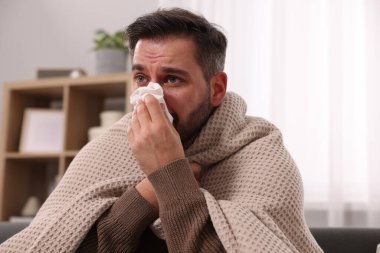 Hasta adam battaniyeye sarılı ve evdeki kanepede burnunu siliyor. Soğuk belirtileri